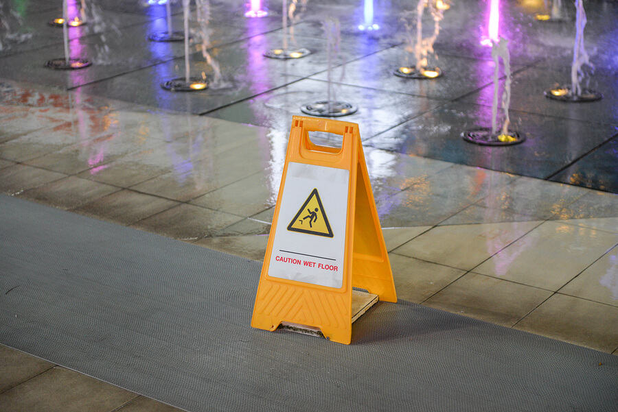 Fountains and a wet sidewalk in Charleston, West Virginia with a sign to help prevent slip and fall accidents.