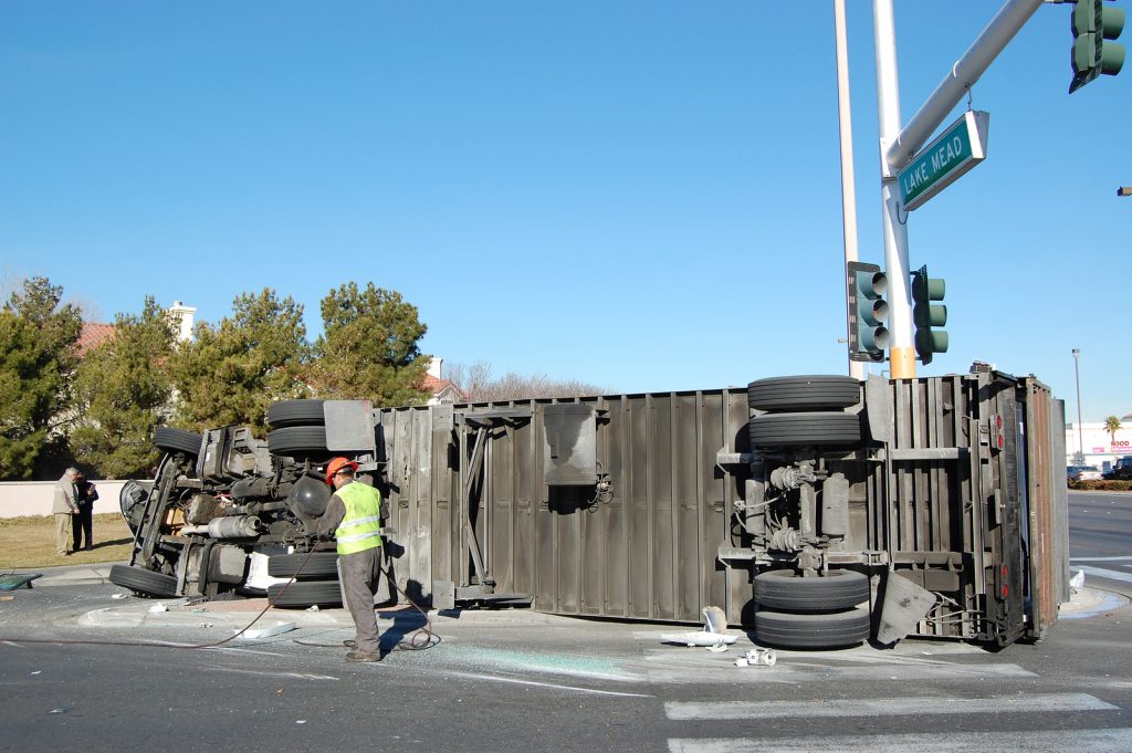 Intersection accident with an overturned truck and a person calling an 18-wheeler accident lawyer on their cell phone.